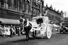 Andrew Hauge driving the Dalagar Grocery float with Mr. and Mrs. Dalagar riding down Austin's Main Street (1930)